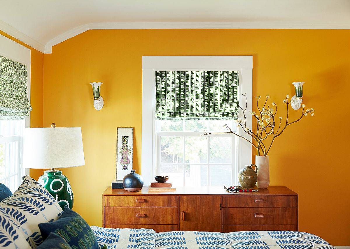 Bức tường màu vàng quyến rũ kết hợp với rèm cửa sổ màu xanh lá và ga gối xanh lam trong phòng ngủ phong cách chiết trung.