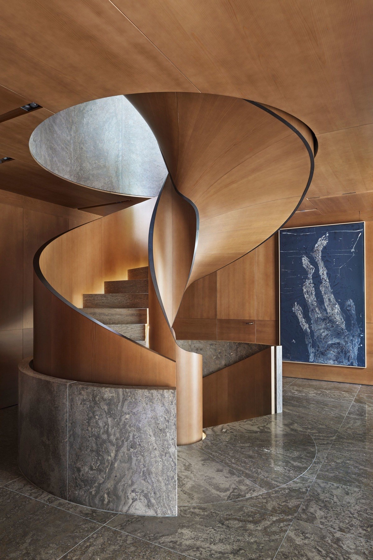 Bức tường đá tròn bao quanh cầu thang giúp tôn lên hiệu ứng tương phản giữa chất liệu gỗ ấm áp với đá màu xám.