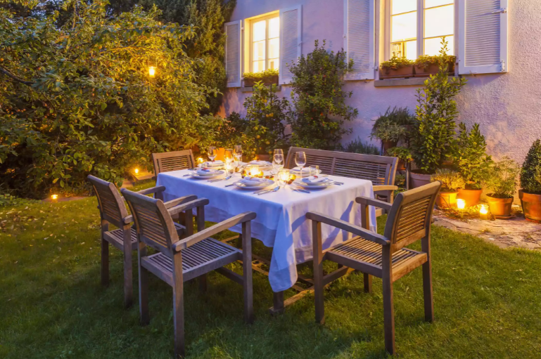 Trang trí bàn tiệc mùa thu ngoài trời với khăn trải bàn màu trắng, hoa hoặc quả mọng màu cam theo mùa và đèn lồng ấm áp.